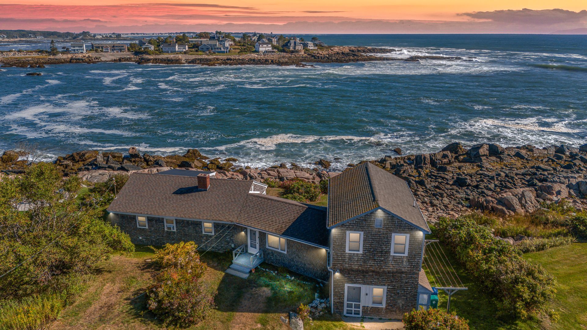 Coastal house overlooking rocky shore and choppy ocean at sunset