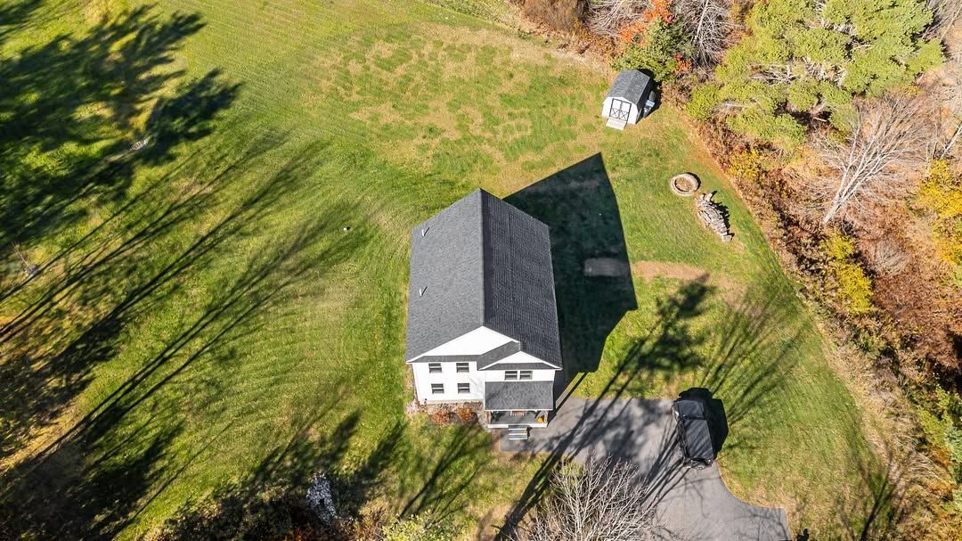 Aerial view of a white house with a dark roof on a grassy lot, with trees and a driveway nearby