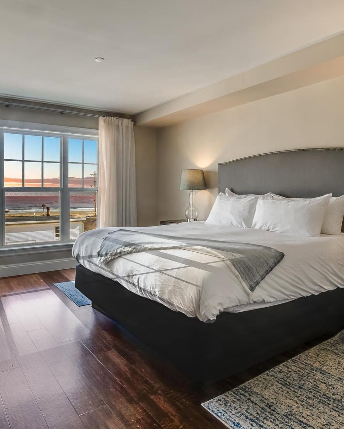 Modern bedroom with a large bed, gray headboard, window view, and warm neutral decor