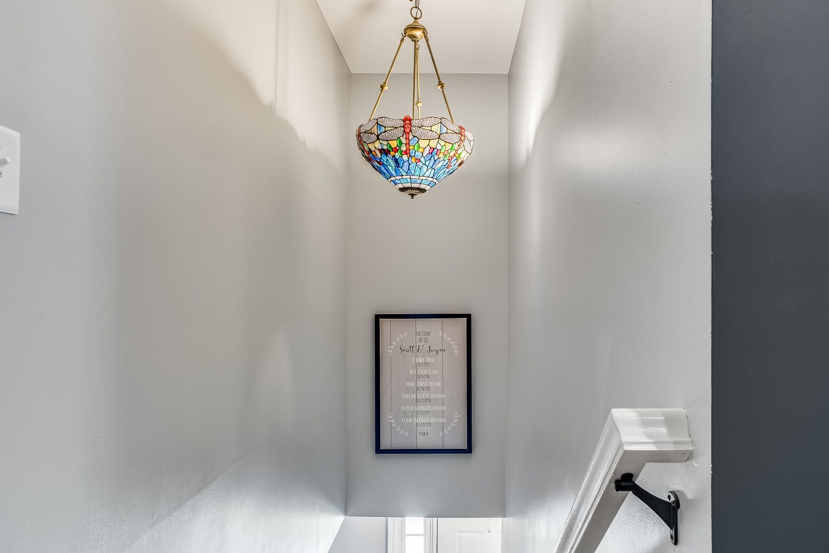 Narrow stairwell with a colorful hanging chandelier and framed print on the far wall