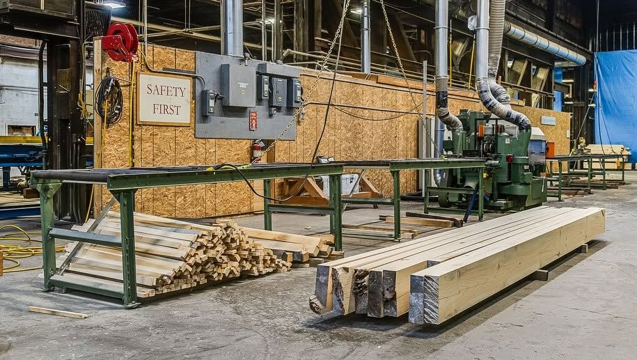 Lumber mill with stacked timber boards and industrial machinery in a workshop.