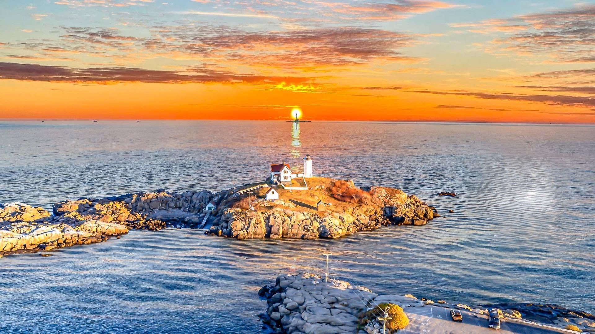 Sunset over a rocky jetty with a lighthouse, glowing orange sky and calm blue ocean