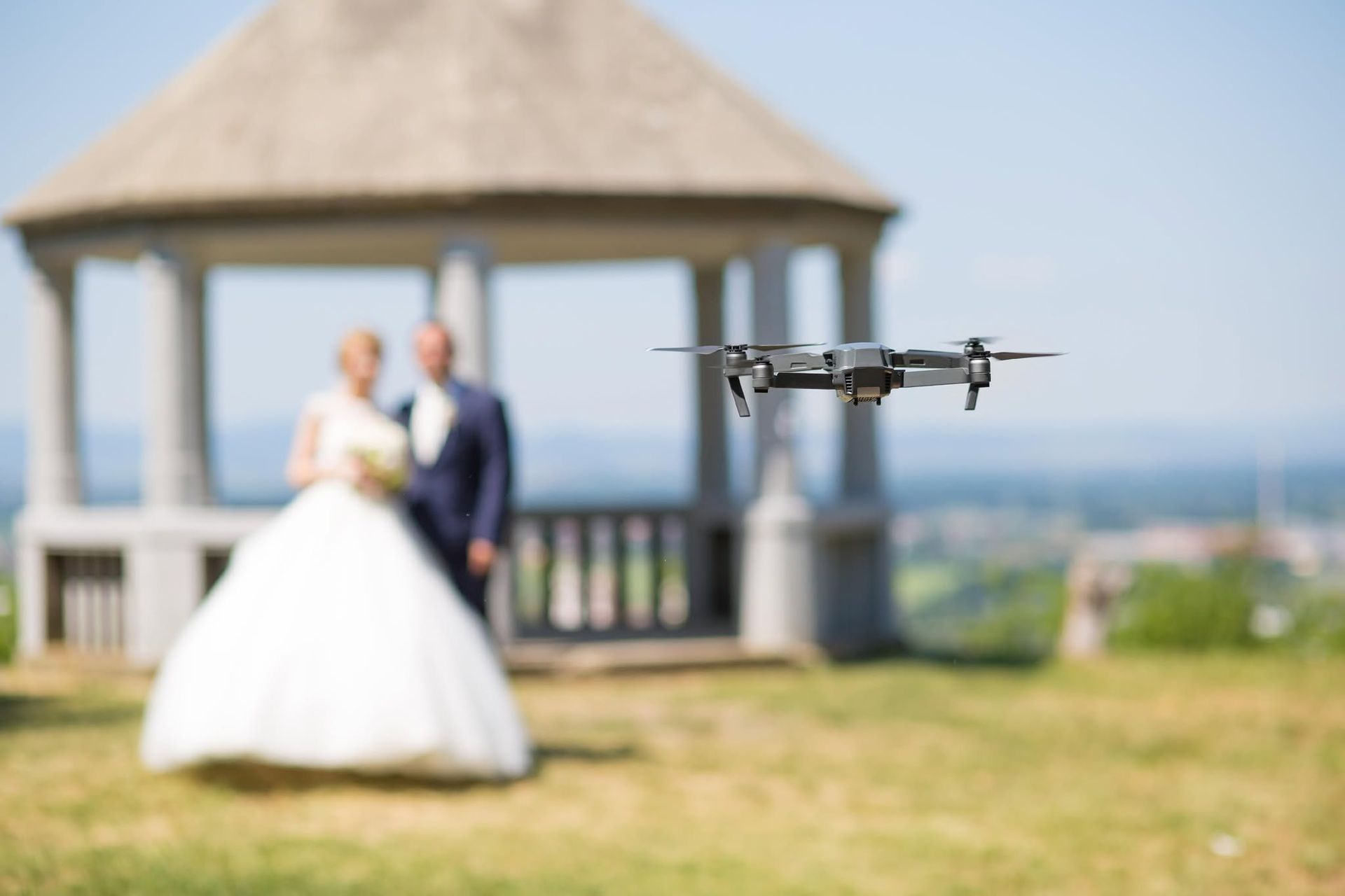 Drone flying in front of a blurred bride and groom at an outdoor gazebo
