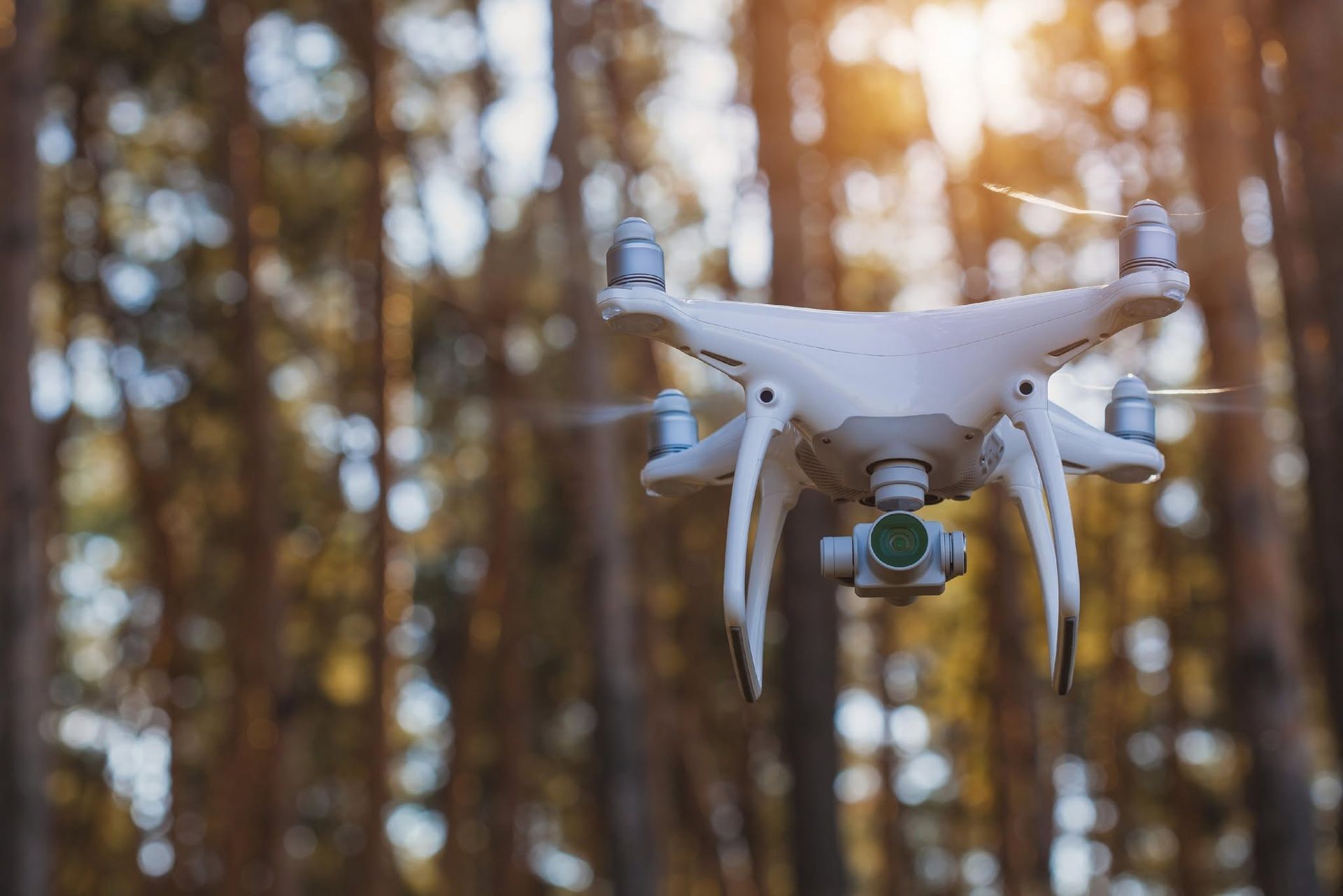 White drone flying in a blurred forest at sunset