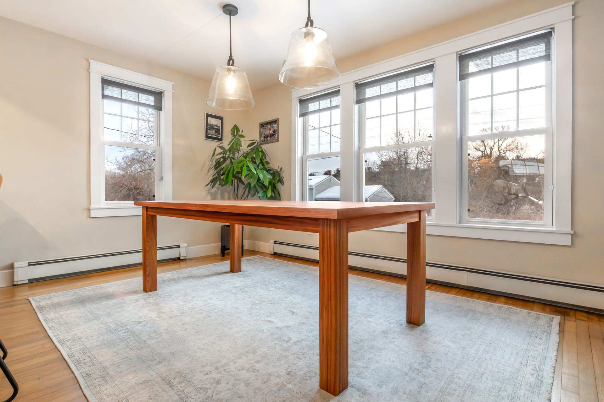 Bright dining room with wooden table, large windows, pendant lights, and a pale rug