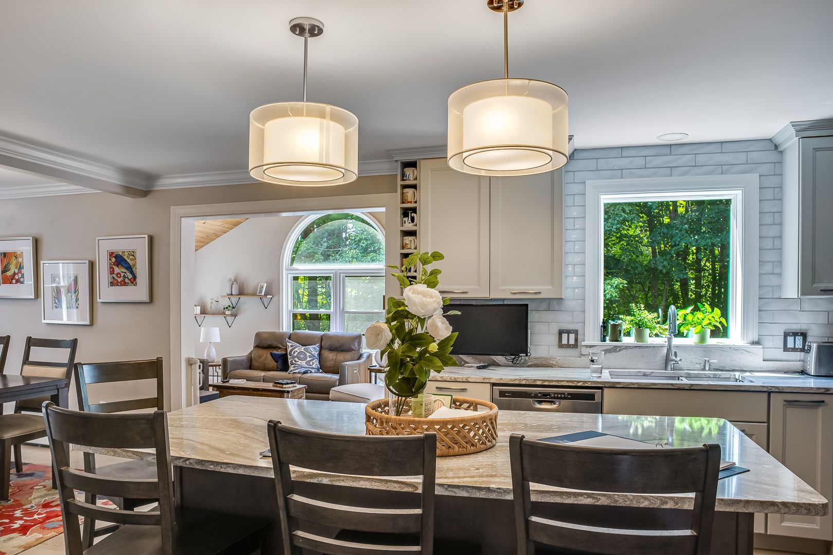 Modern kitchen and dining area with island, pendant lights, and large windows overlooking greenery