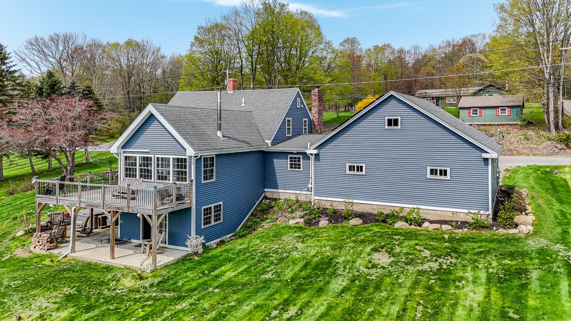 Blue two-story house with gray addition, deck, and lush green lawn under a sunny sky