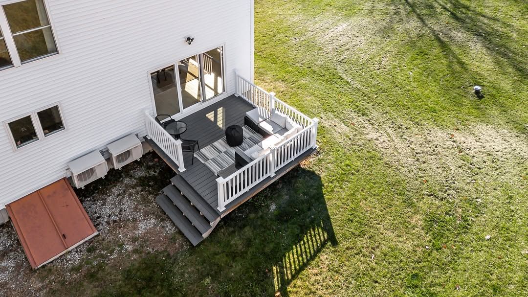 Aerial view of a white house deck with stairs, patio furniture, and a grassy yard