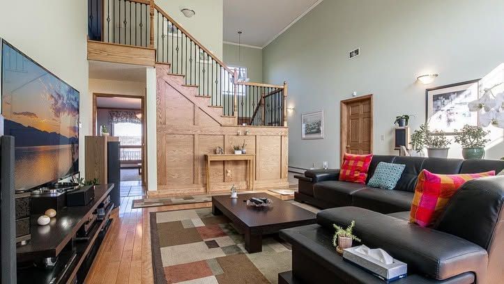 Modern living room with black sectional, glass coffee table, staircase, and large wall art