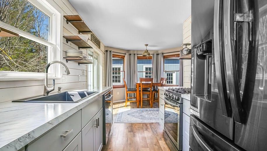 Bright kitchen with white cabinets, black fridge, and open view to a dining area with wood table and chairs
