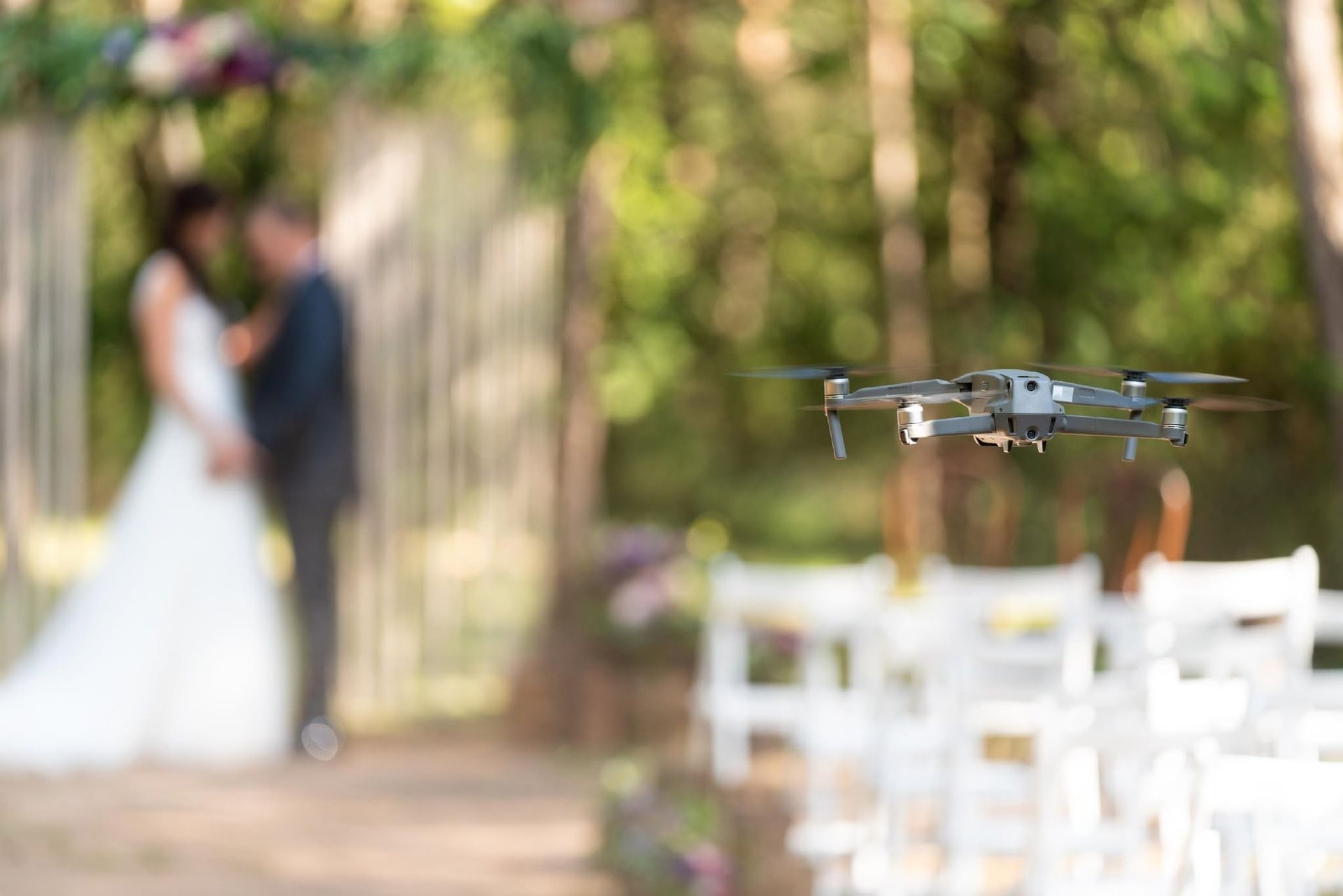Drone hovering at an outdoor wedding ceremony with a blurred bride and groom in the background