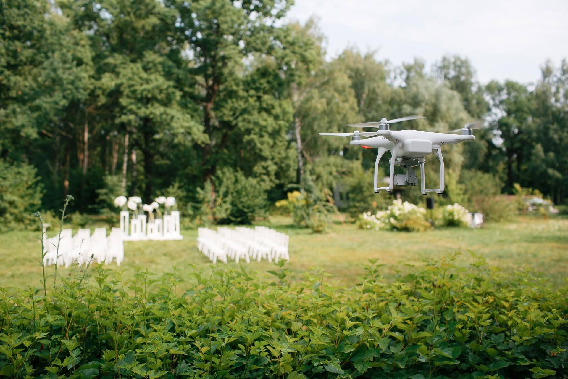 Drone hovering over a white outdoor wedding setup in a green garden