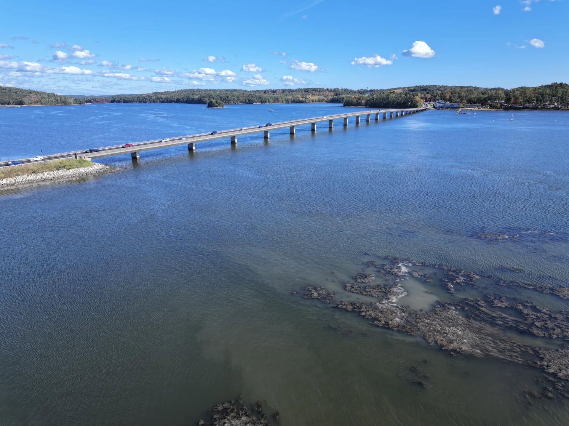 Shallow blue bay with a long wooden walkway or breakwater extending into the water under a sunny sky