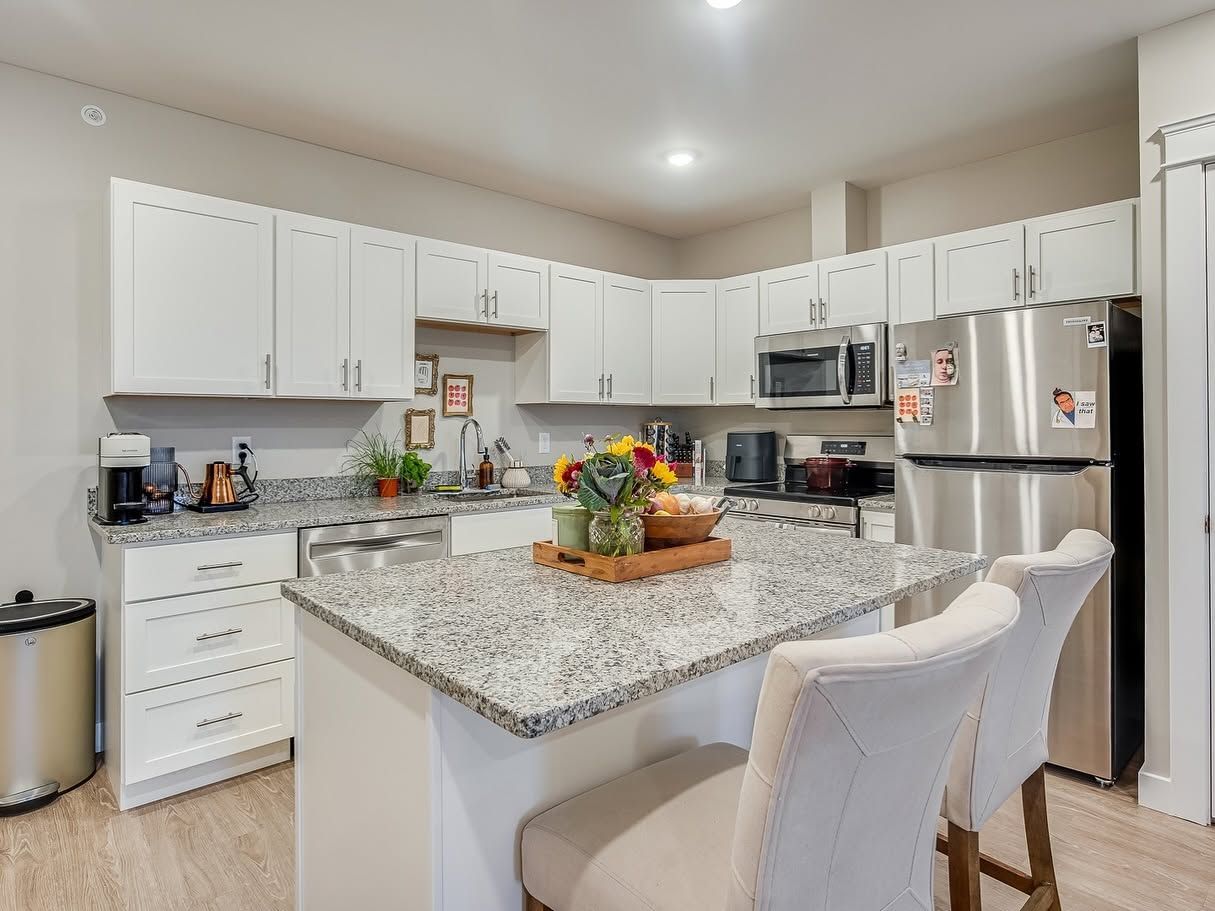 Bright white kitchen with granite island, stainless steel appliances, and two cream bar stools