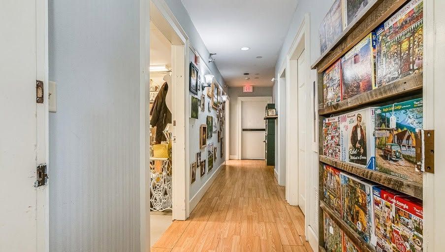 Bright hallway with wooden floors, white walls, and colorful framed art on the right side.