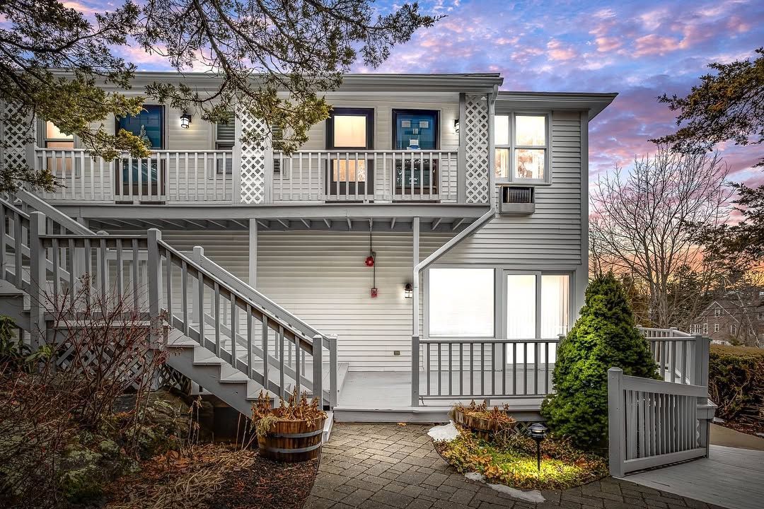 Two-story gray house with front porch, balcony, and exterior stairs at sunset