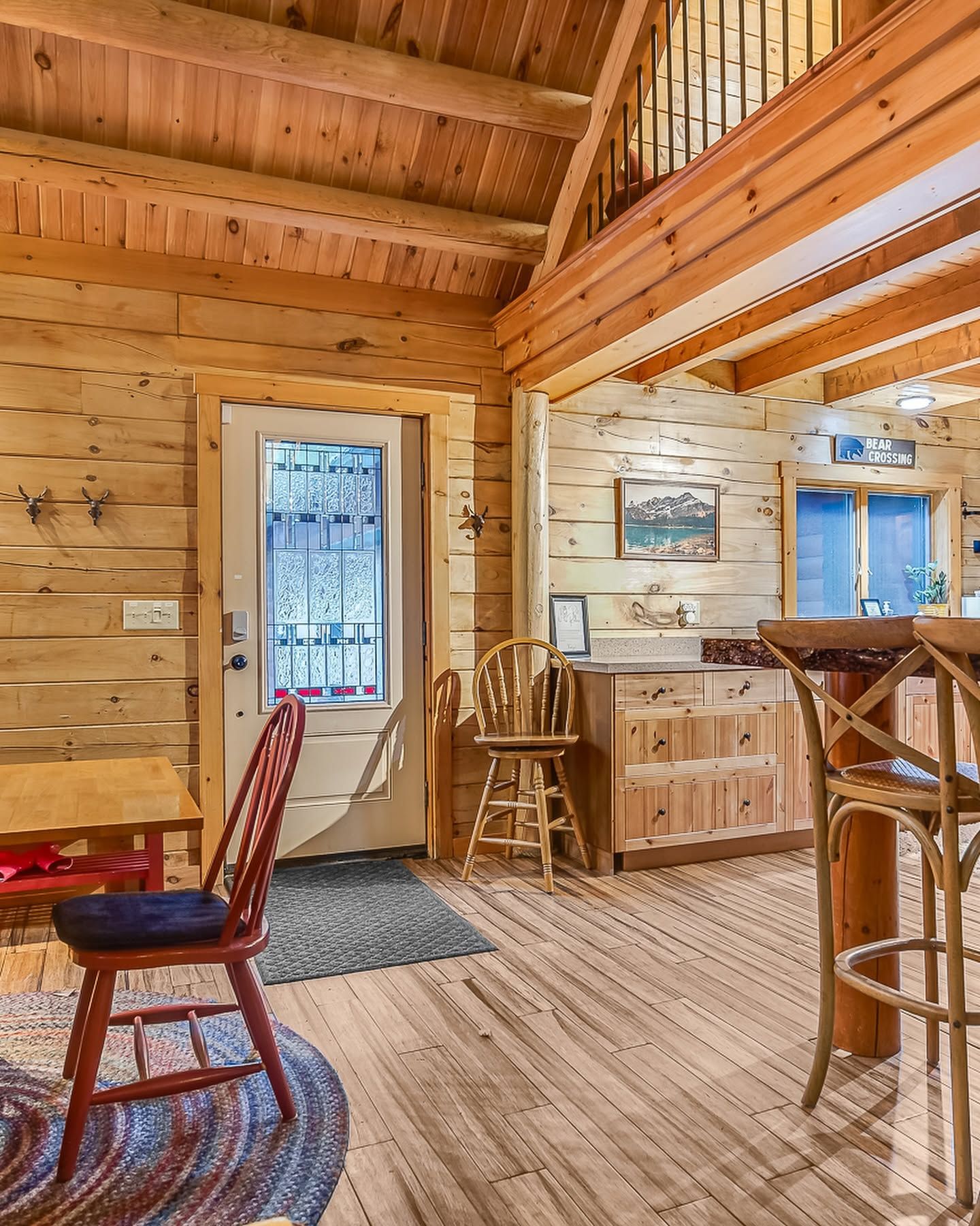 Cozy wooden cabin interior with red chair, bar stools, door, and sunlit window
