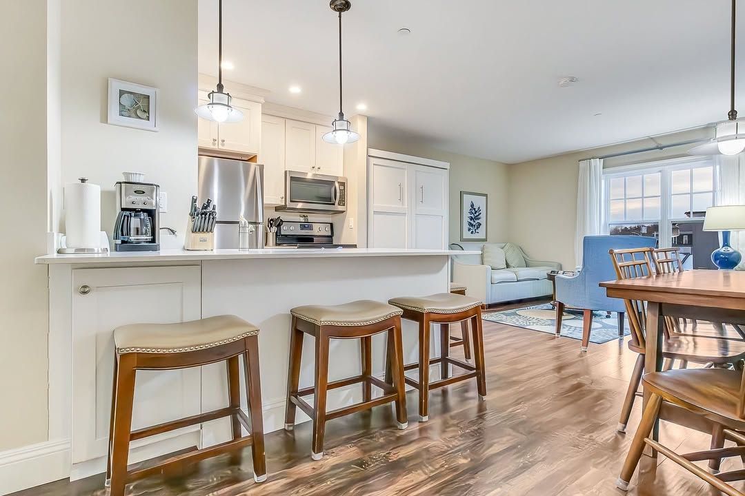 Bright open kitchen with white island, bar stools, pendant lights, and hardwood floors, leading to a dining area