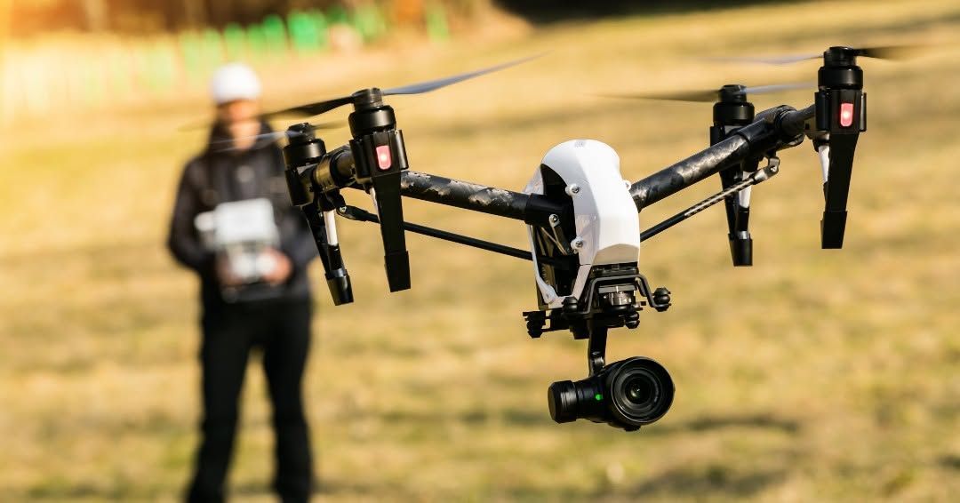 Large black drone hovering in a field with a blurred person standing behind it