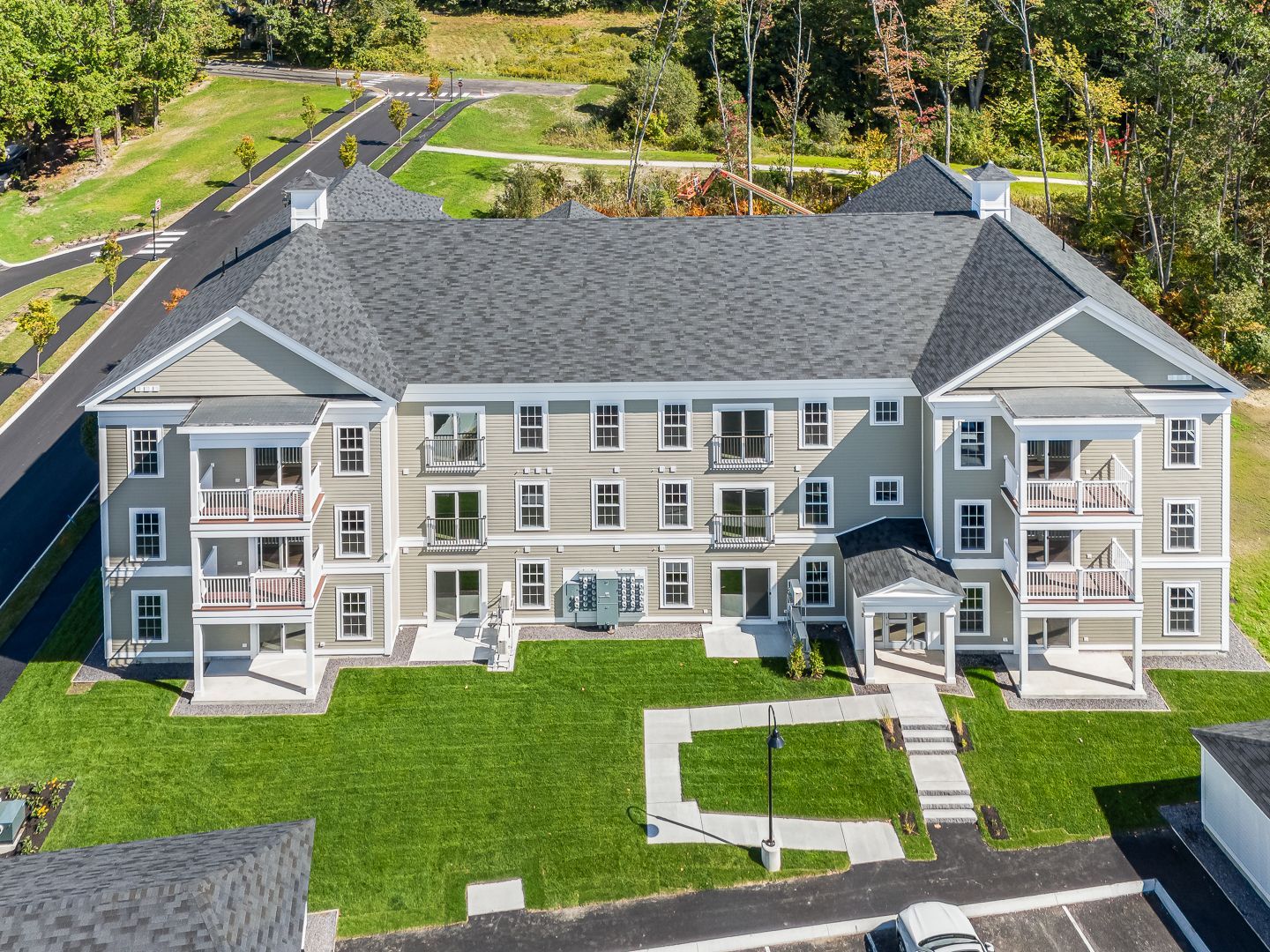 Aerial view of a gray apartment building with green lawn, walkways, and surrounding trees.