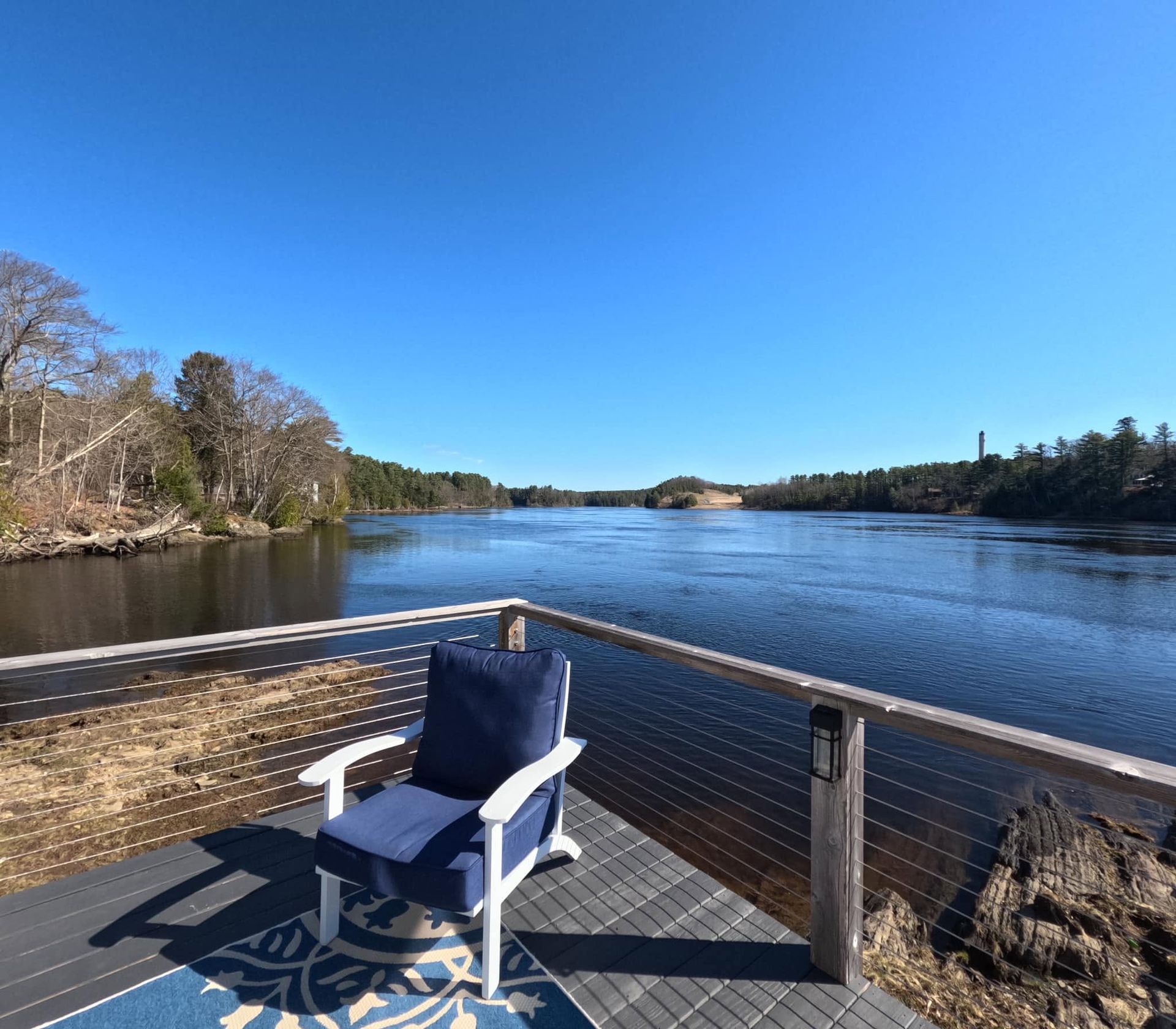 Blue chair on a wooden deck overlooking a calm lake under a clear blue sky.
