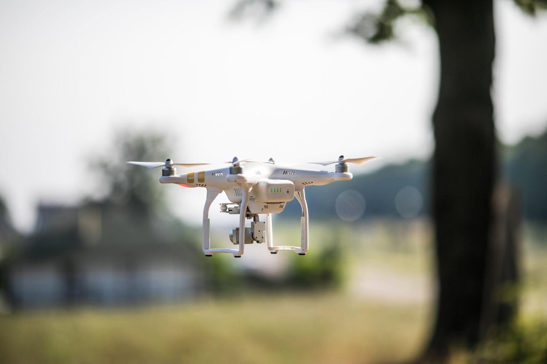 White quadcopter drone flying outdoors against a blurred park-like background