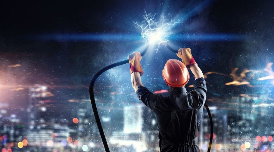 Worker in hard hat welding overhead at a glowing construction site at night