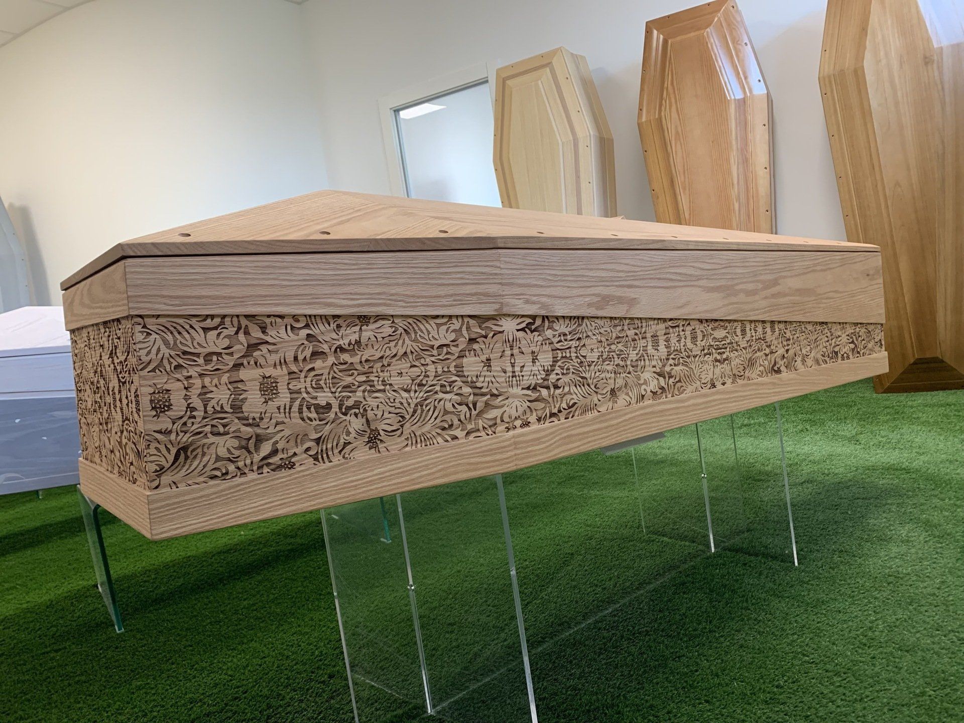 Una bara di legno è posta in cima a un prato verde in una stanza.