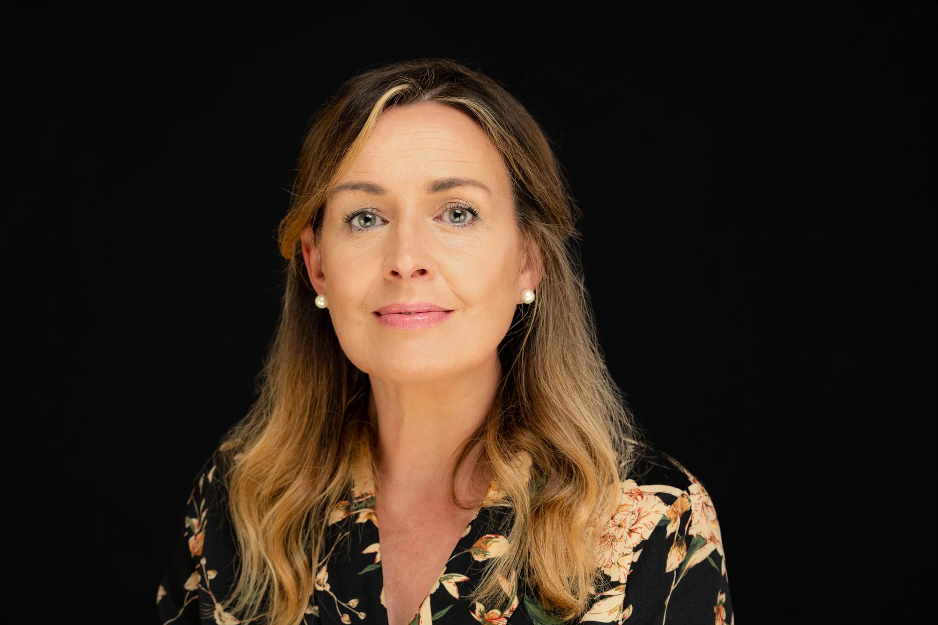 Portrait of a woman with long brown hair against a black background, wearing a floral blouse
