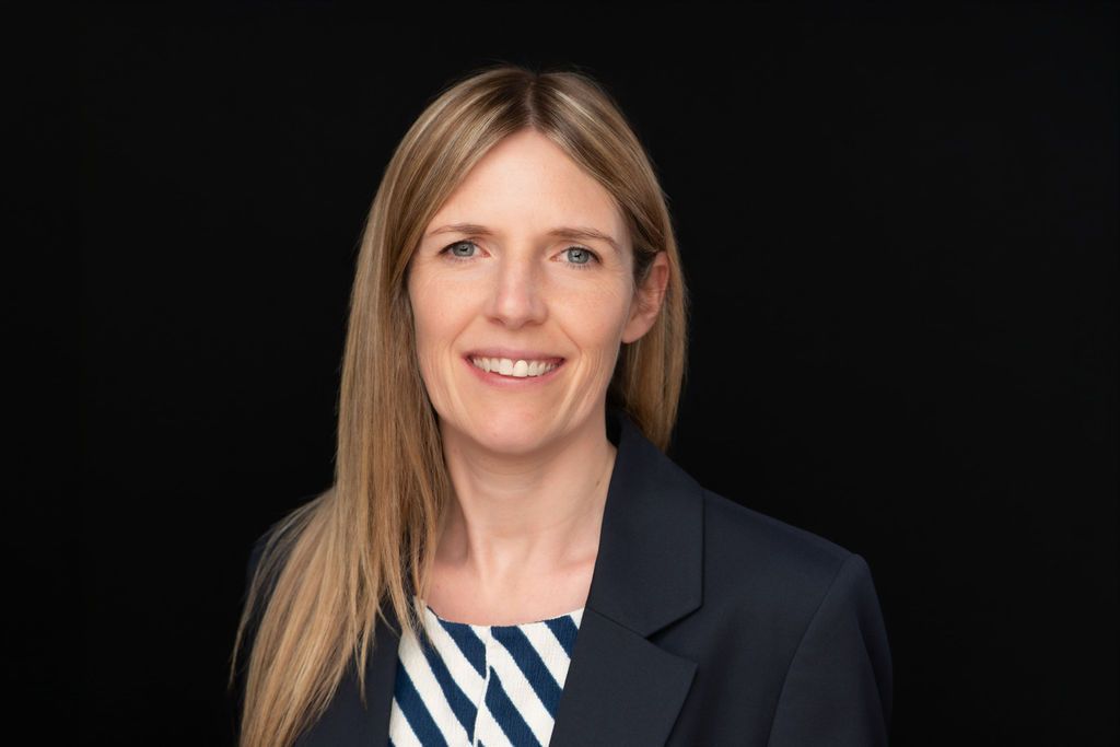 Portrait of a smiling woman in a dark blazer and striped top against a black background