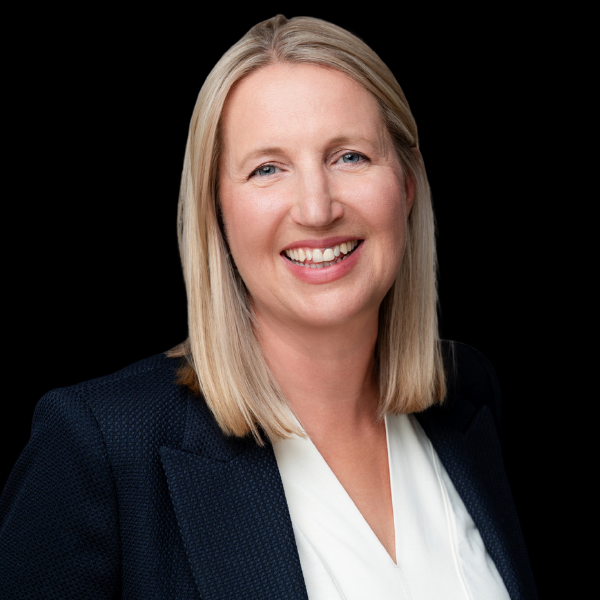 Smiling blonde professional in a dark blazer and white blouse against a black background