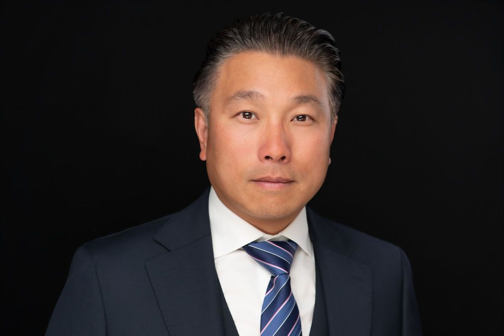 Studio portrait of a man in a dark suit and striped tie against a black background