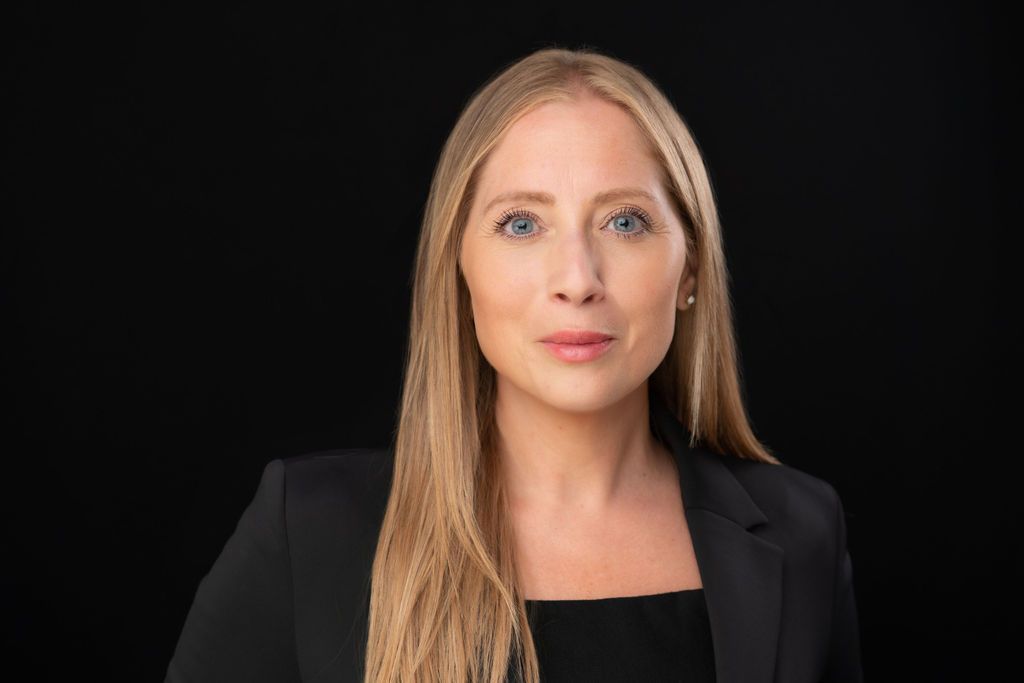 Portrait of a person with long blonde hair wearing a black blazer against a black background