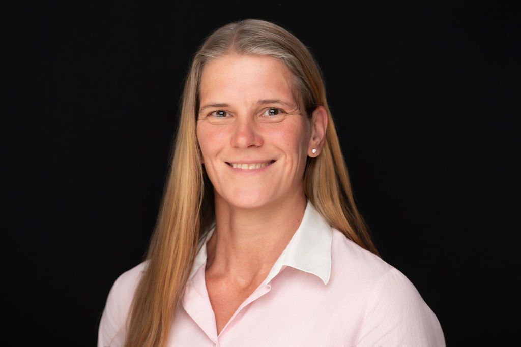 Portrait of a smiling person with long blonde hair wearing a light pink shirt on a black background