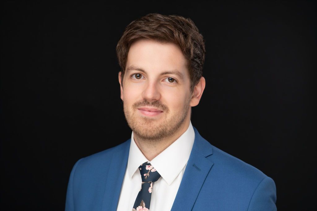 Studio portrait of a person in a blue suit and white shirt against a black background