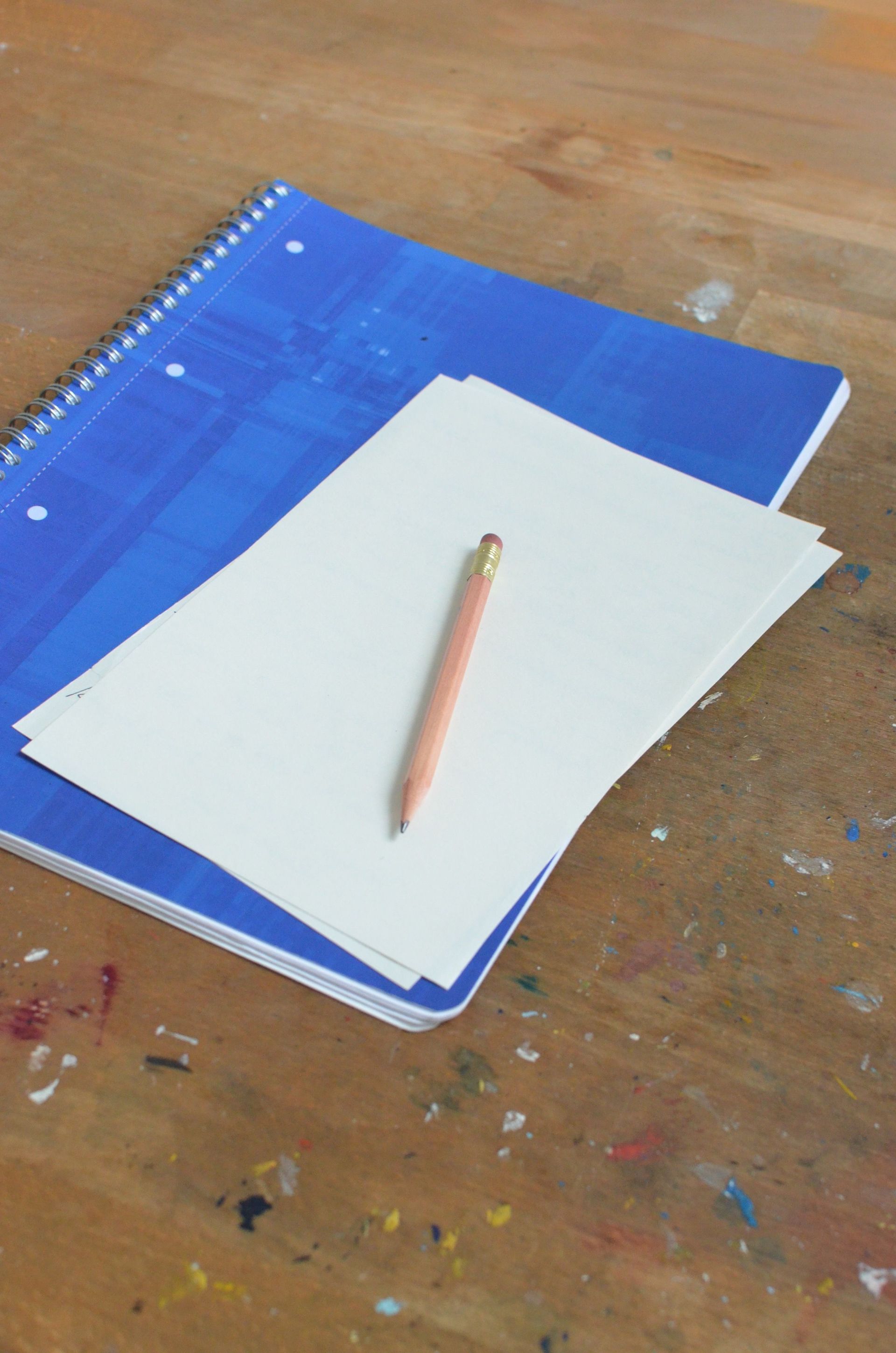 White paper and pencil on a blue spiral notebook on a wooden table.