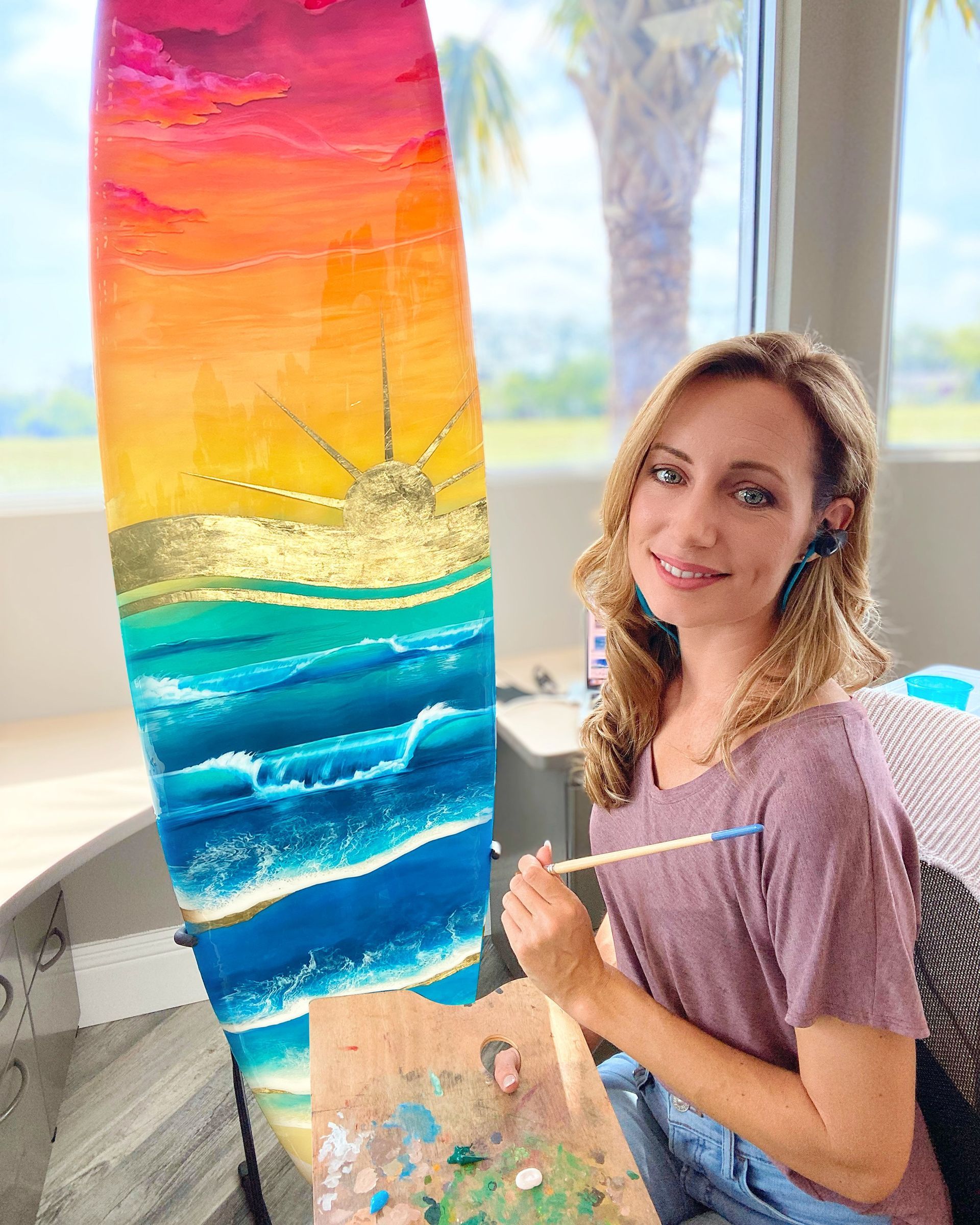 A woman is painting a surfboard with a brush.