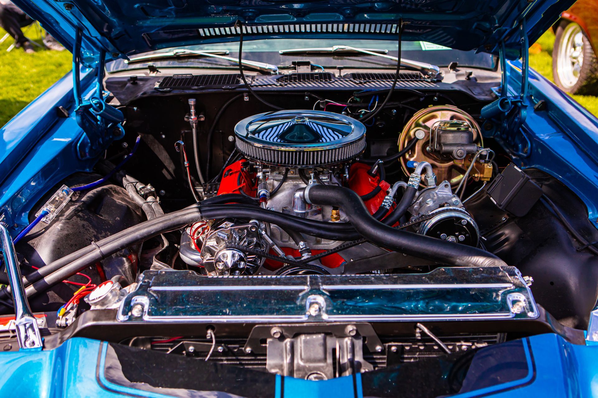 Classic blue car with hood open, showing a polished chrome engine bay at a car show Classic blue car with hood open, showing a polished chrome engine bay at a car show