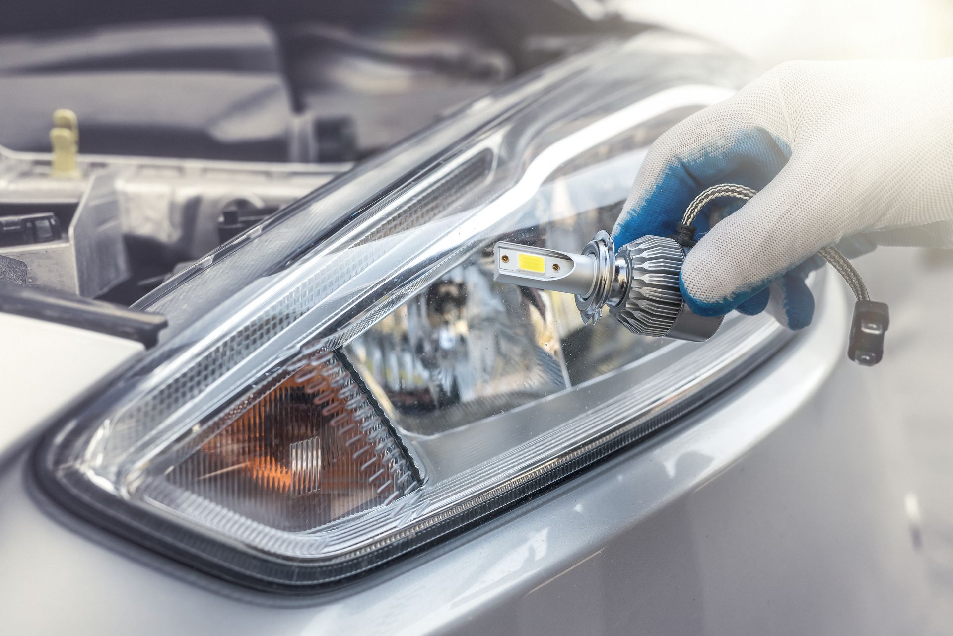 Gloved hand installing an LED bulb into a car headlight assembly