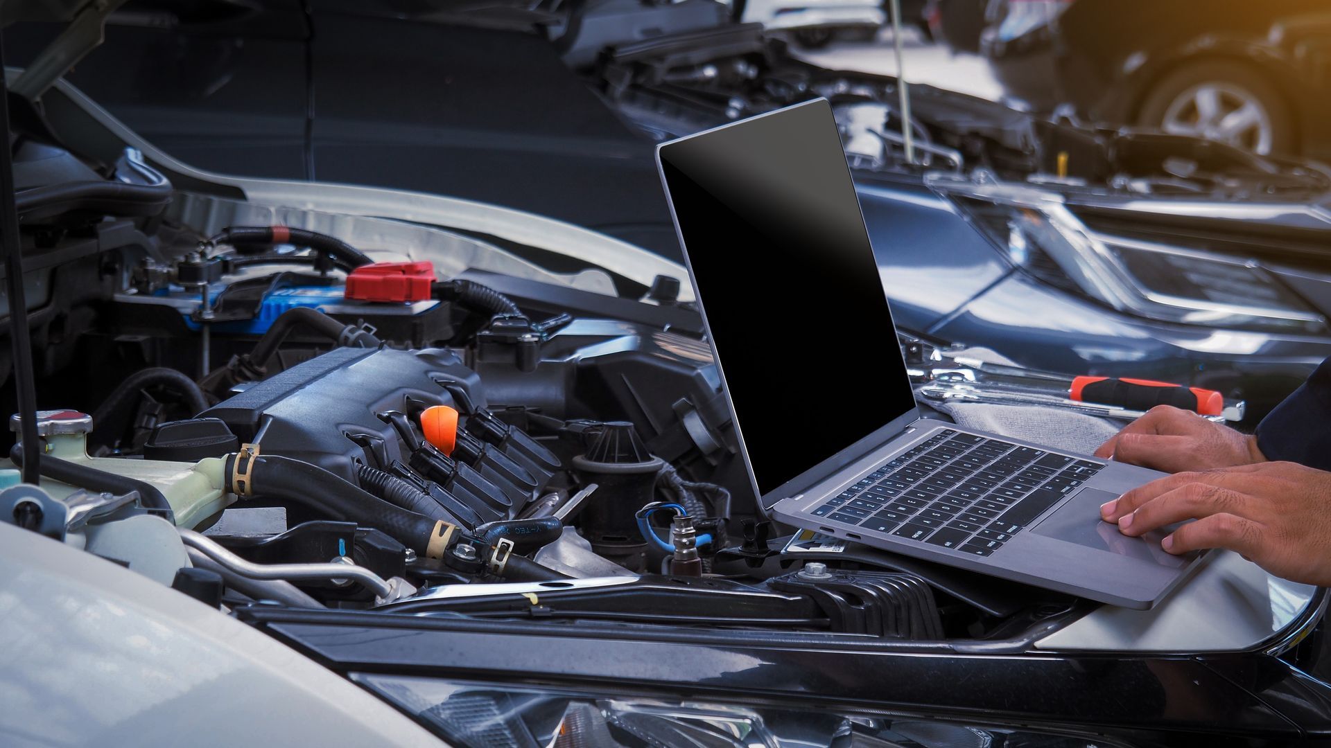 Mechanic using a laptop to diagnose a car engine under the hood