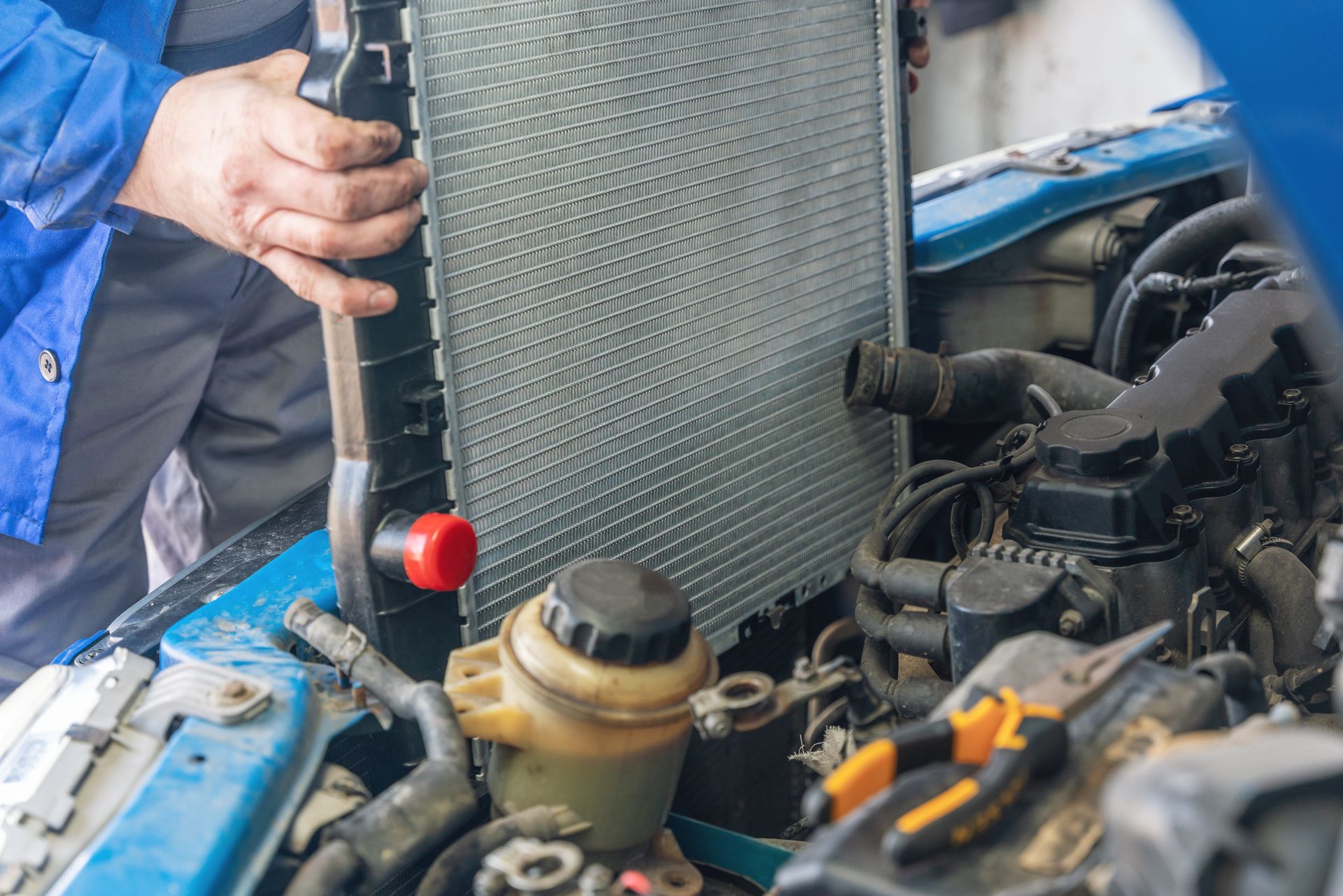 Mechanic working under a car hood, checking the engine with tools visible.