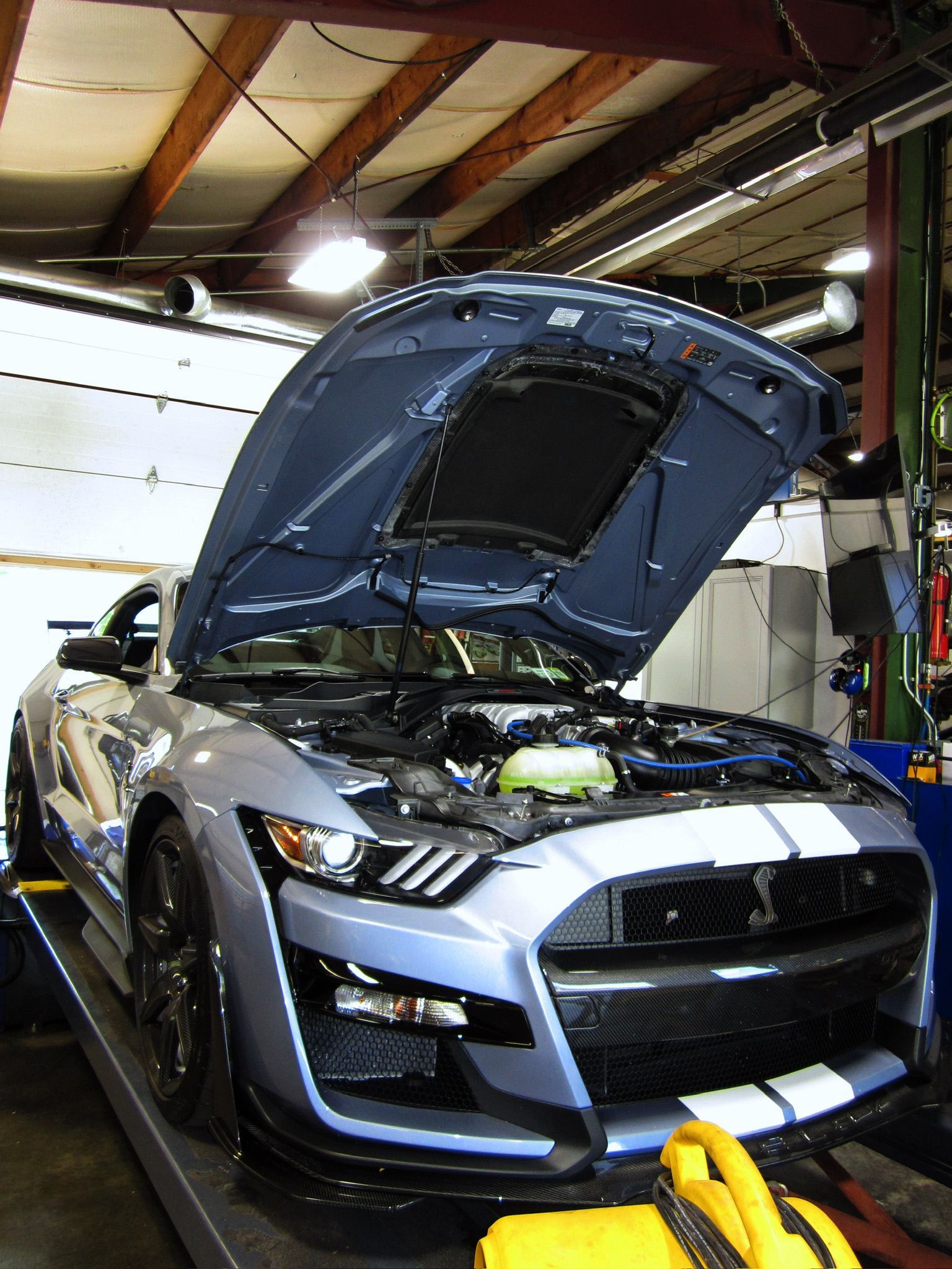 Blue sports car with hood open in a garage, showing the engine compartment.