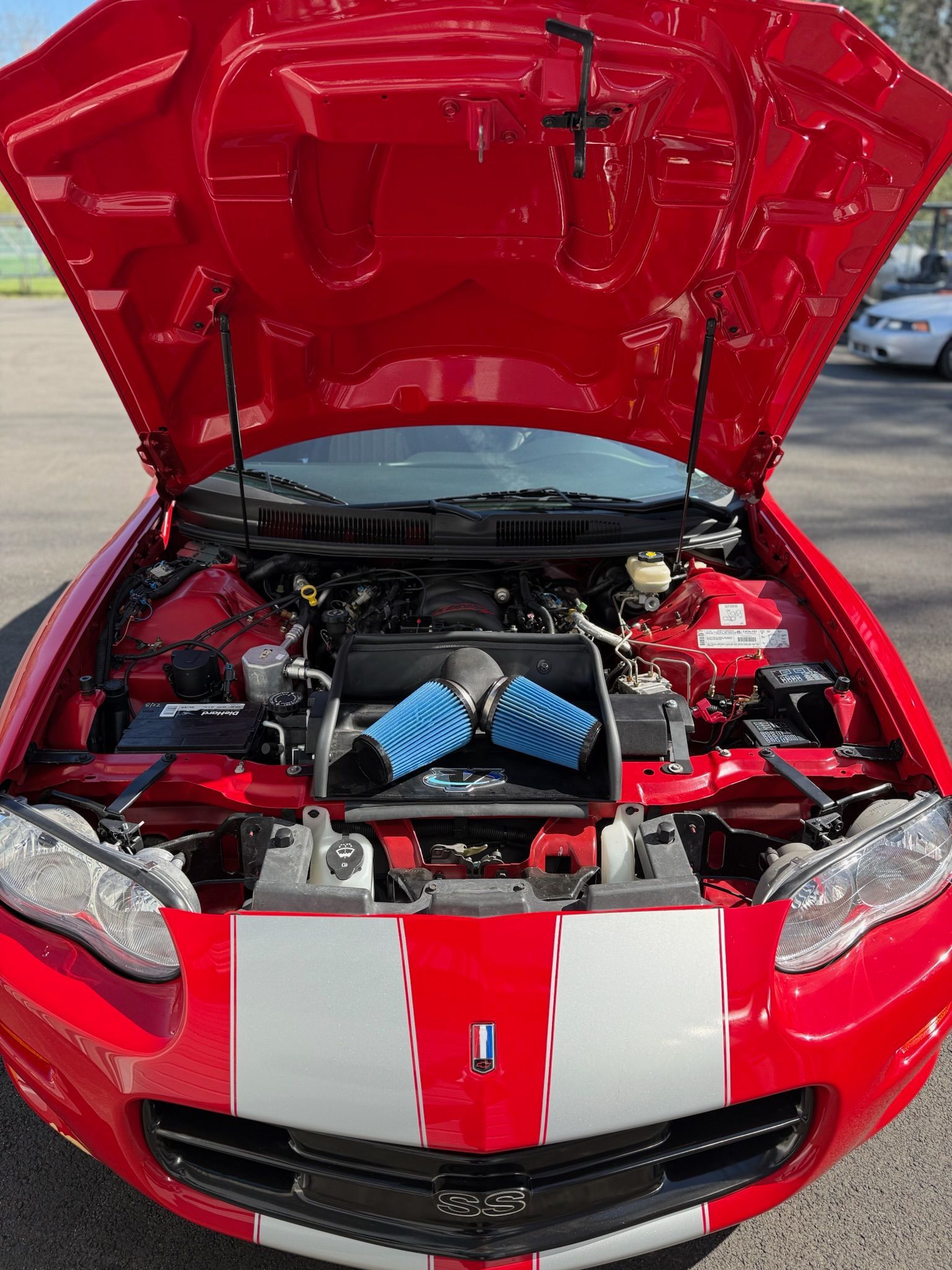 Red sports car with hood open, showing engine bay and twin blue cone air filters.