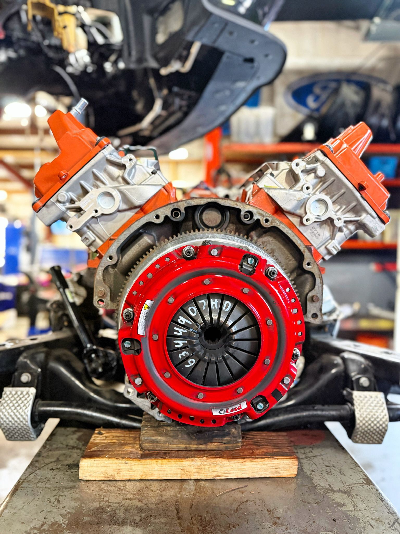 Red engine or transmission assembly on a workbench in a garage, with orange and silver components.