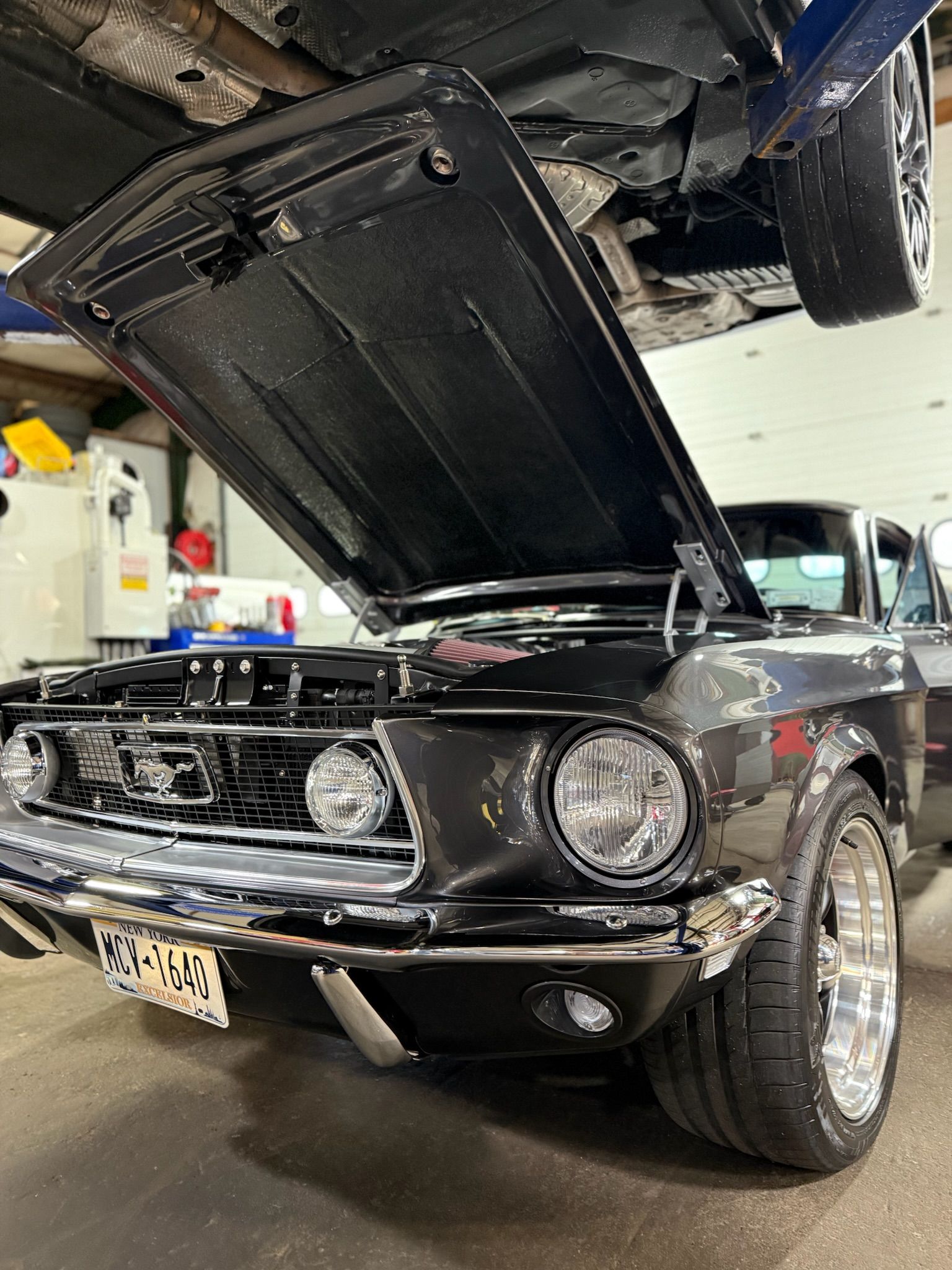 Black classic Mustang in a garage with hood open, front view showing chrome grille and round headlights