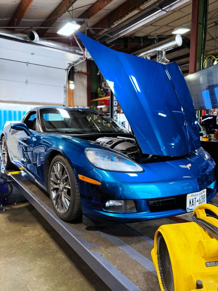 Blue sports car in a garage with its hood open, showing engine maintenance.