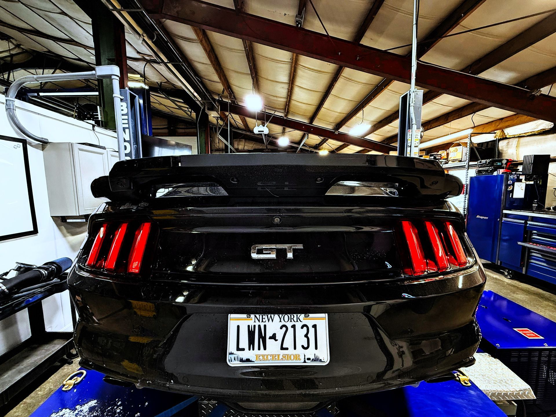 Black sports car on a service lift in a garage, rear view with red taillights and a license plate visible