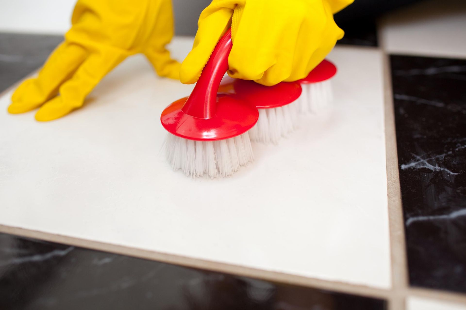 a person in yellow gloves cleaning a tile floor