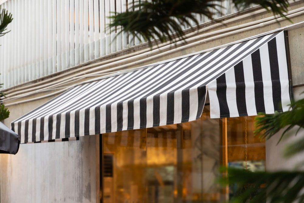 A Black and White Striped Awning is on the Side of a Building  — Budget Screens & Awnings in Casino, NSW