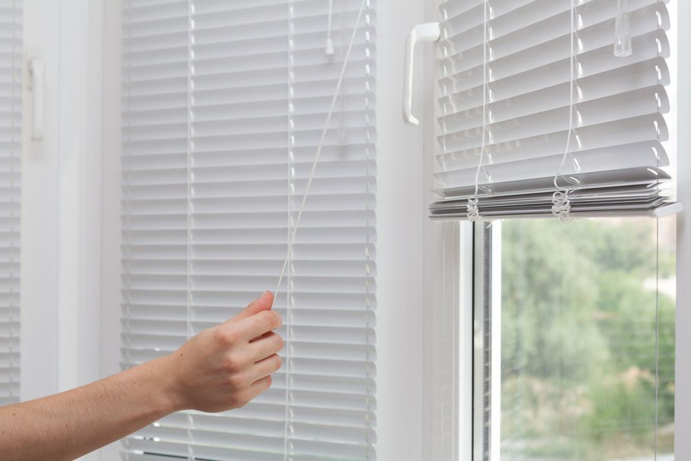 A Person is Opening a Window With Blinds on It — Budget Screens & Awnings in Evans Head, NSW